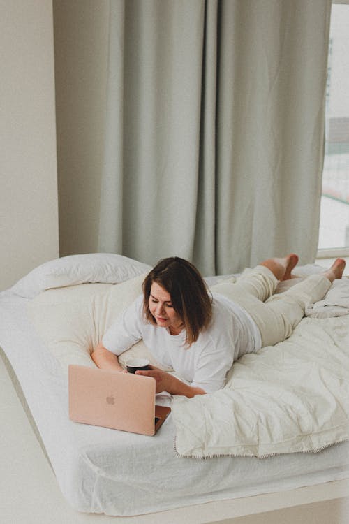 Woman Lying in Bed with Laptop and Cup of Coffee