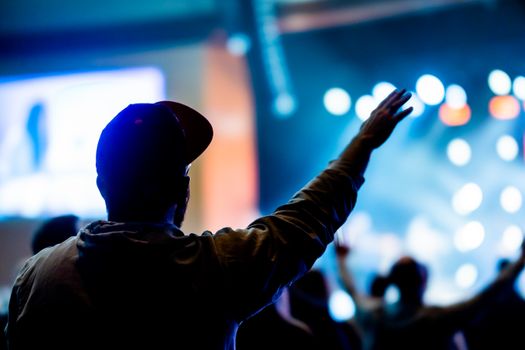 Silhouetted figure raising arm in lively concert with electric lights.