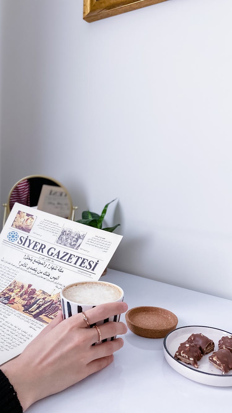 A Hand Holding A Cup Of Coffee And Newspaper