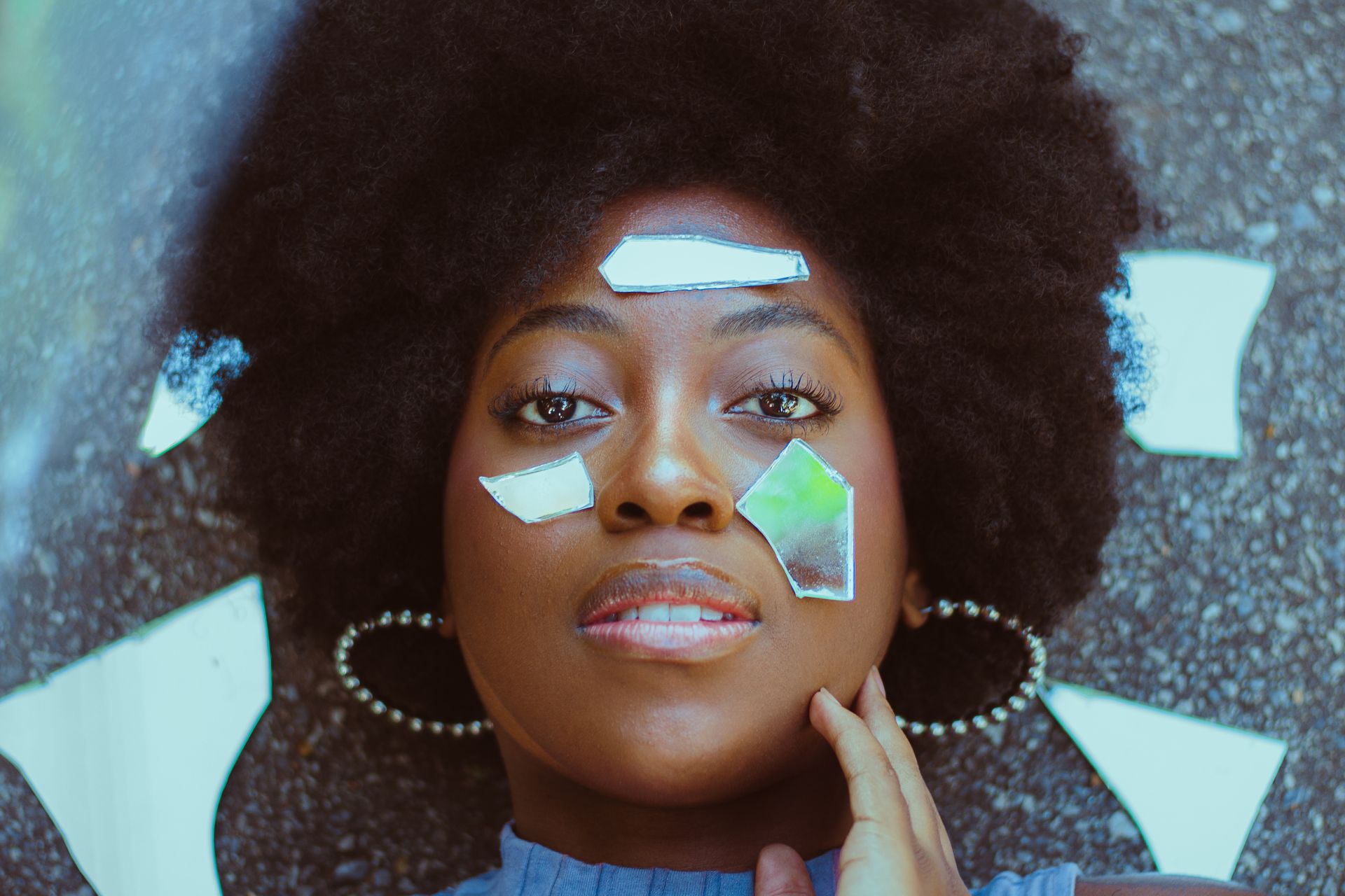 Artistic photo of woman lying with mirror pieces on her face.