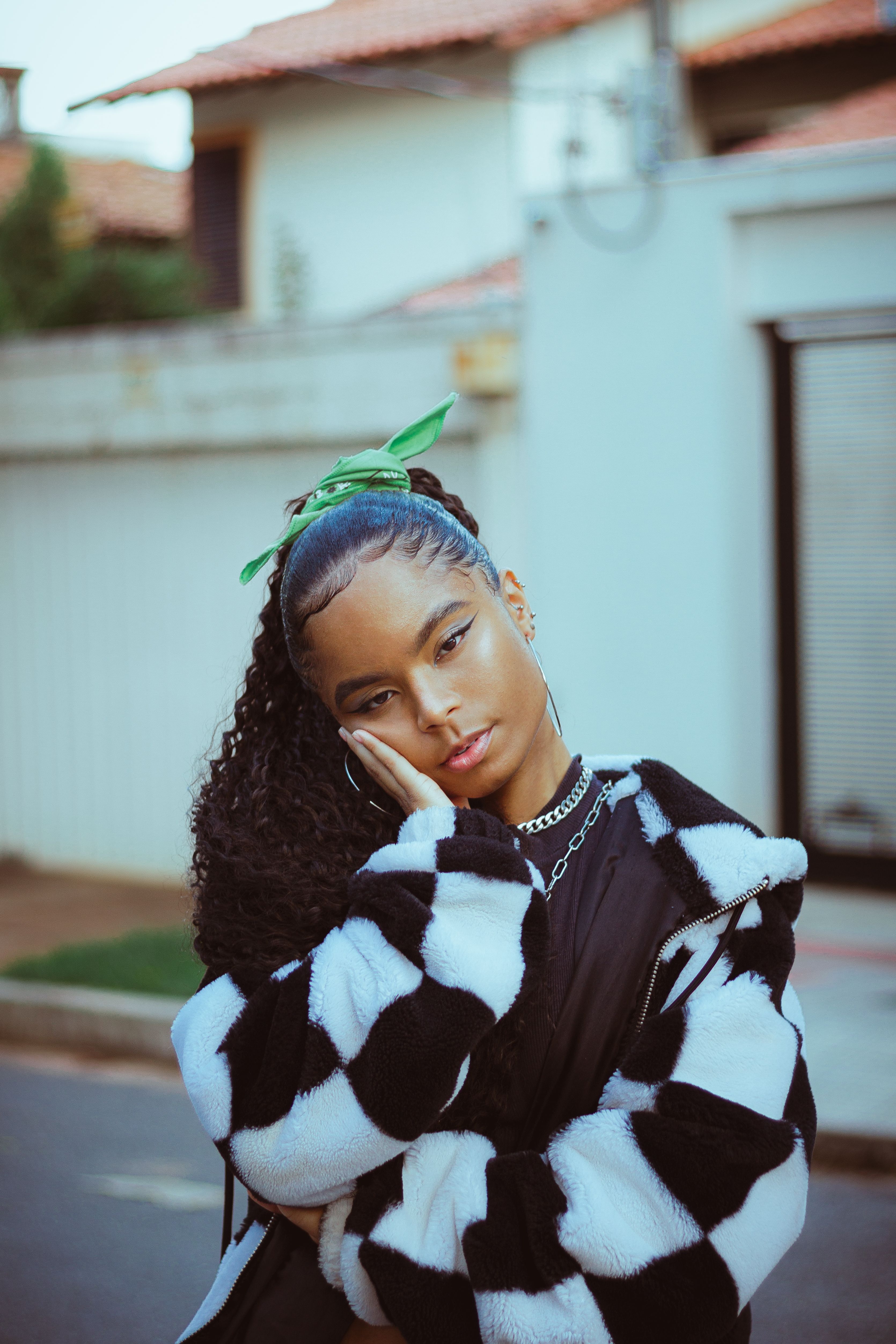 Portrait of a stylish woman with curly hair posing outdoors in a checkered jacket, exuding confidence and elegance.