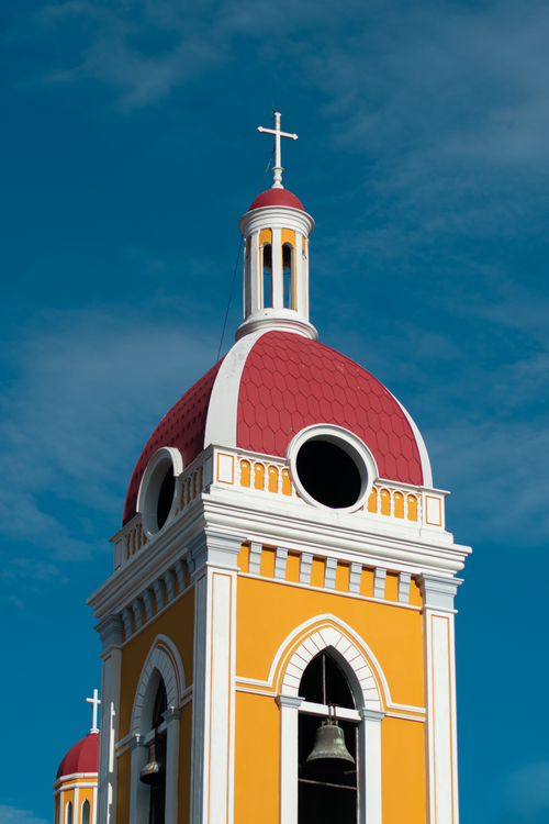 Free Close-up of a vibrant church tower with dome and cross in Nicaragua under a blue sky. Stock Photo