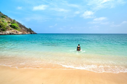 A person wades into a serene turquoise ocean on a sunny tropical beach.