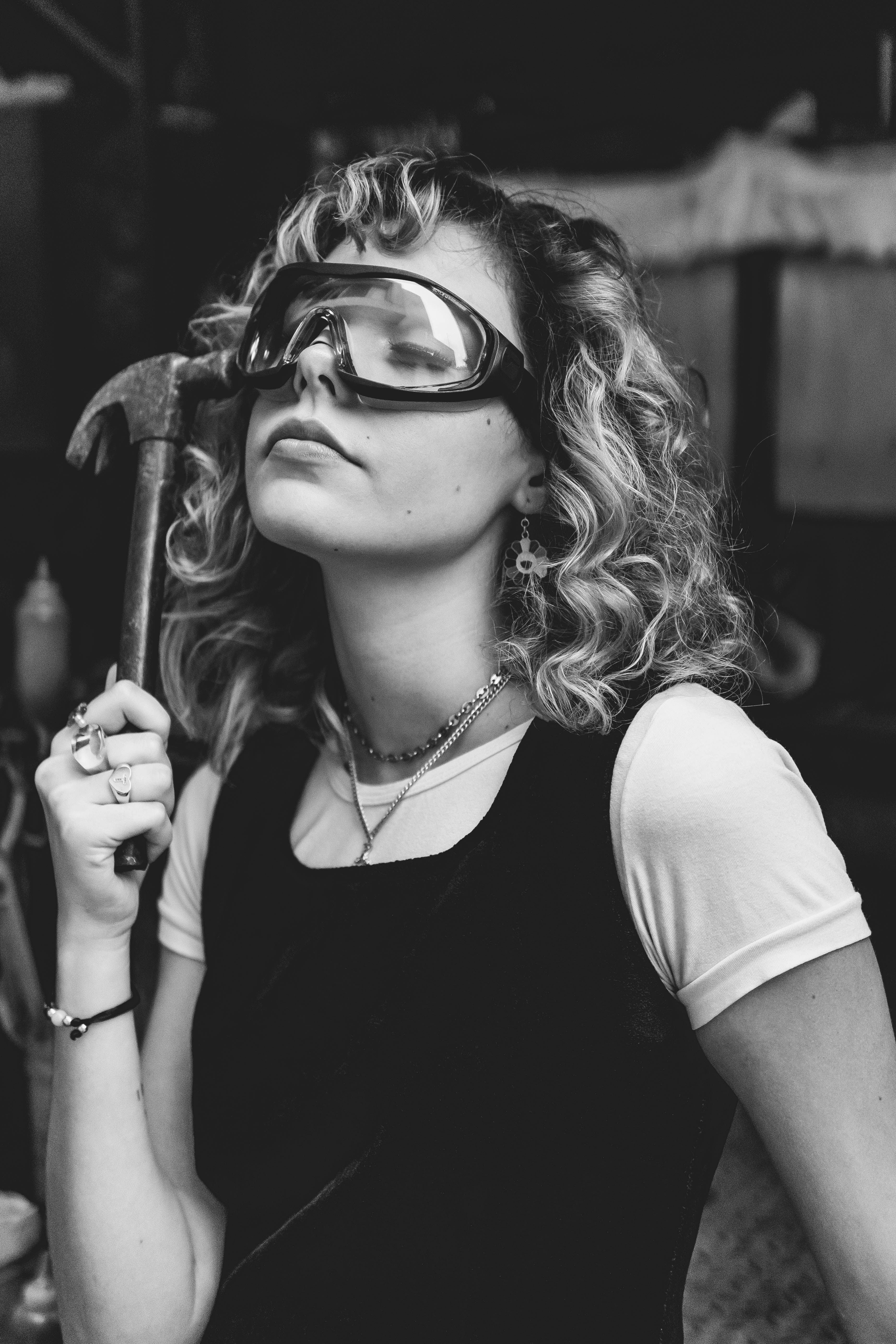 Stylish black and white portrait of a woman wearing goggles and holding a hammer.