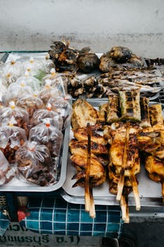 A variety of grilled Asian street food including chicken and fish skewers on a stainless tray.
