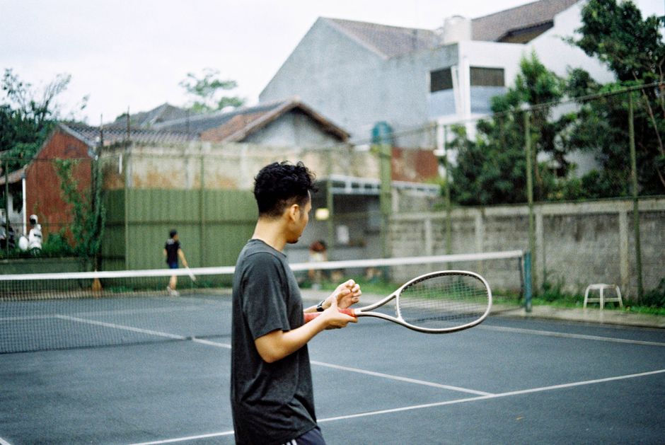 Adult male playing tennis on an outdoor court in Bandung, Indonesia.