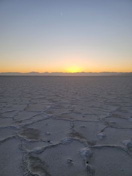 Experience the tranquil beauty of a sunrise over vast salt flats in a serene desert landscape.
