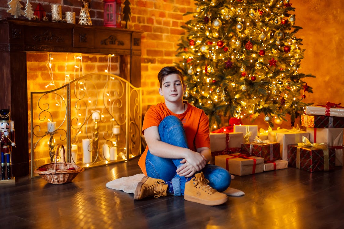 A Boy Sitting near the Christmas Tree and Christmas Gifts