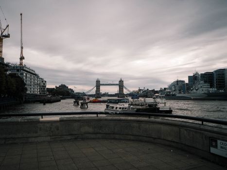 Overcast view of Tower Bridge on the Thames River with ships and city skyline in London.