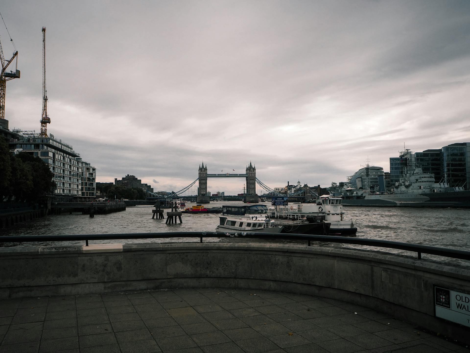 Overcast view of Tower Bridge on the Thames River with ships and city skyline in London.