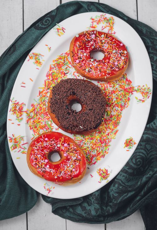 Free Three delectable donuts with vibrant sprinkles served on an elegant white plate, perfect for dessert lovers. Stock Photo