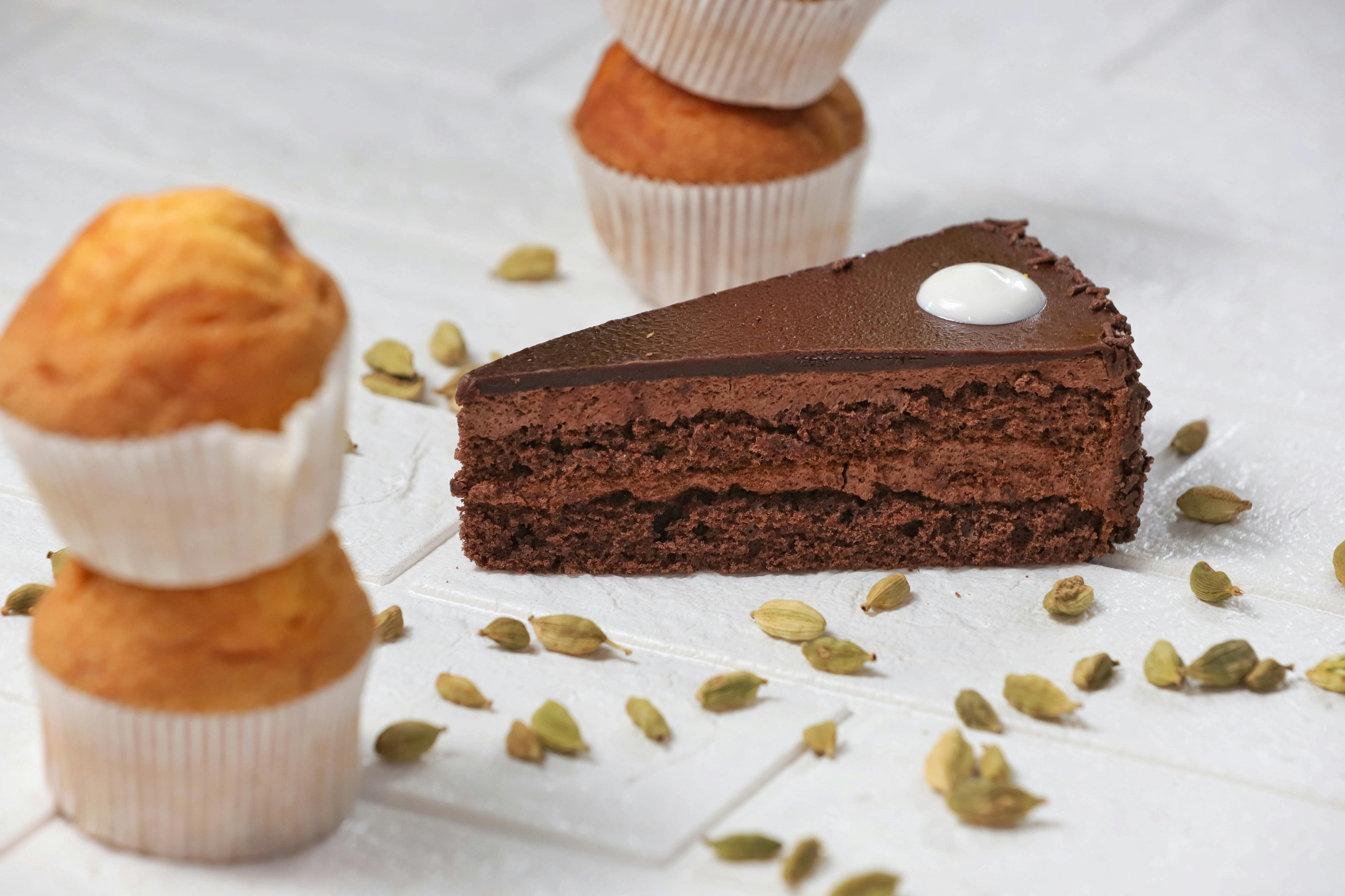 Close-up of a chocolate cake slice, cardamom, and muffins, perfect for dessert lovers.