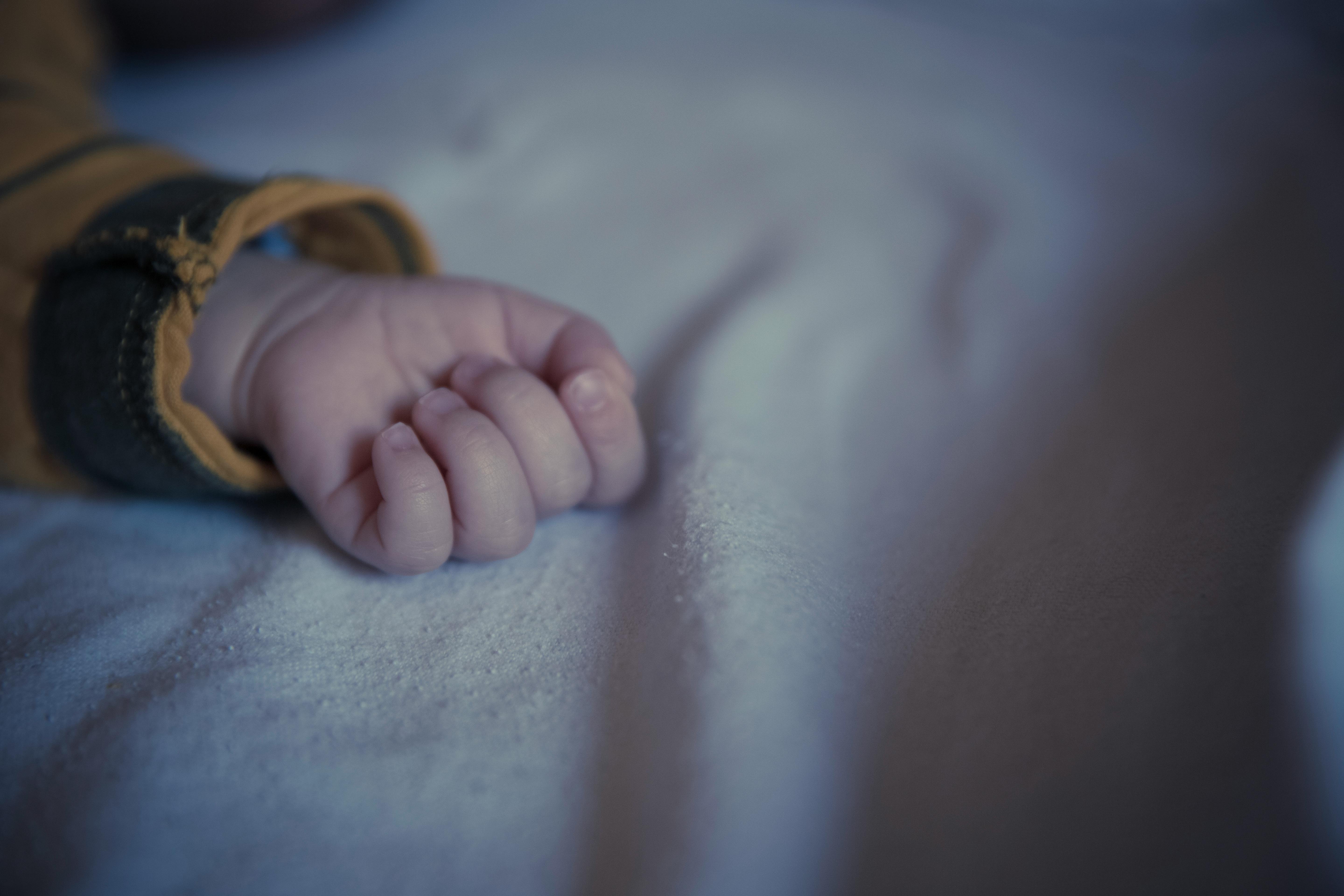 A serene close-up photo of an infant's hand softly resting on a fabric surface.