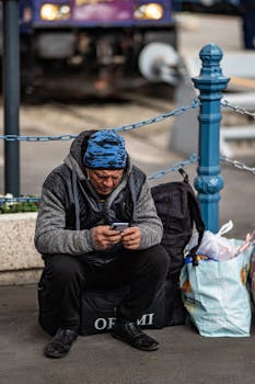 Senior man using phone while sitting with luggage at Budapest train station.