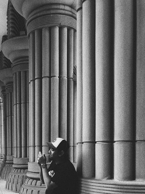 Man leaning on Columns while smoking Cigarette 