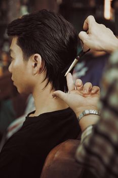 Close-up of a hairstylist giving a haircut to a young man at a salon.