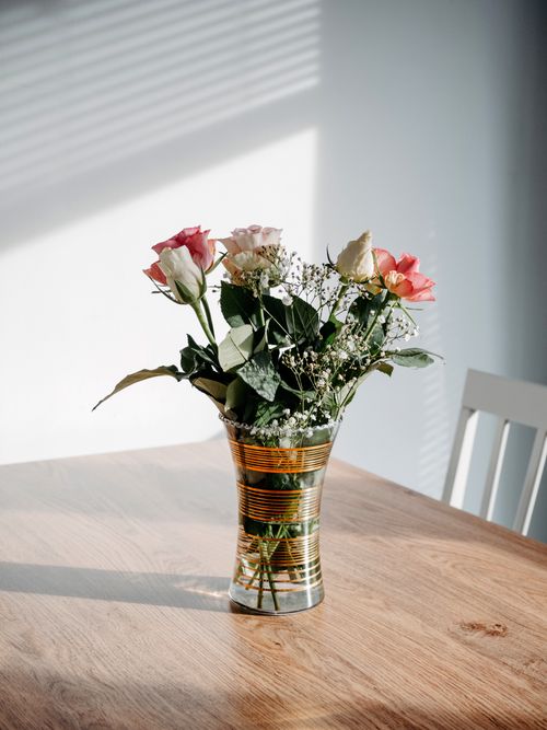 Free A glass vase with roses on a sunlit wooden table in a minimalist dining room. Stock Photo