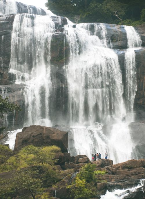 Free Majestic waterfall cascading down rocks in Hasalaka, Sri Lanka, with surrounding lush greenery and tourists observing. Stock Photo