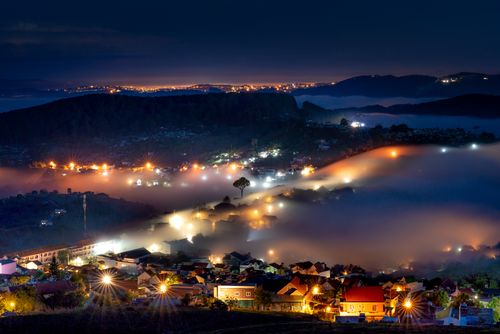 Free Aerial view of a scenic city at night with glowing lights and fog creating a mystical atmosphere. Stock Photo