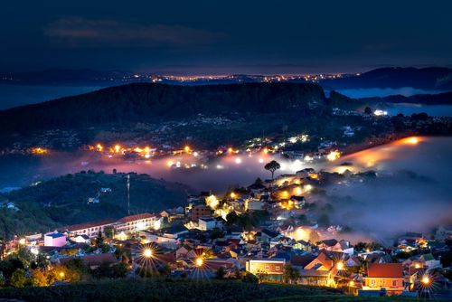 Free A breathtaking aerial view of a city illuminated with lights under a foggy, mountainous backdrop at night. Stock Photo