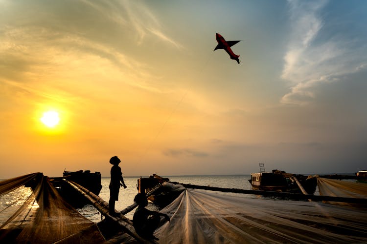 Silhouette Of A Boy Flying A Kite During Sunset