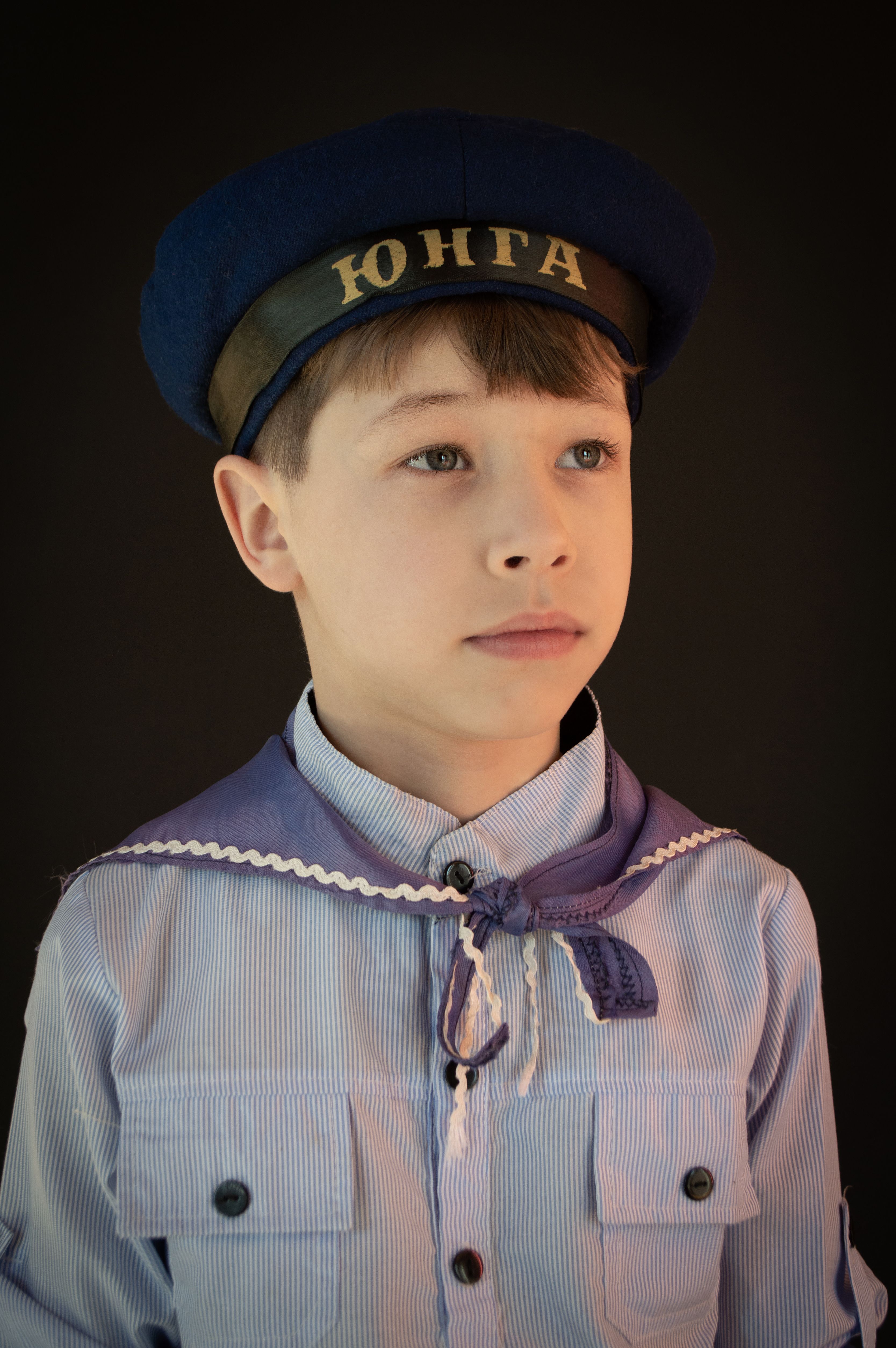 Young boy in naval-inspired attire against a dark background, embodying a classic look.