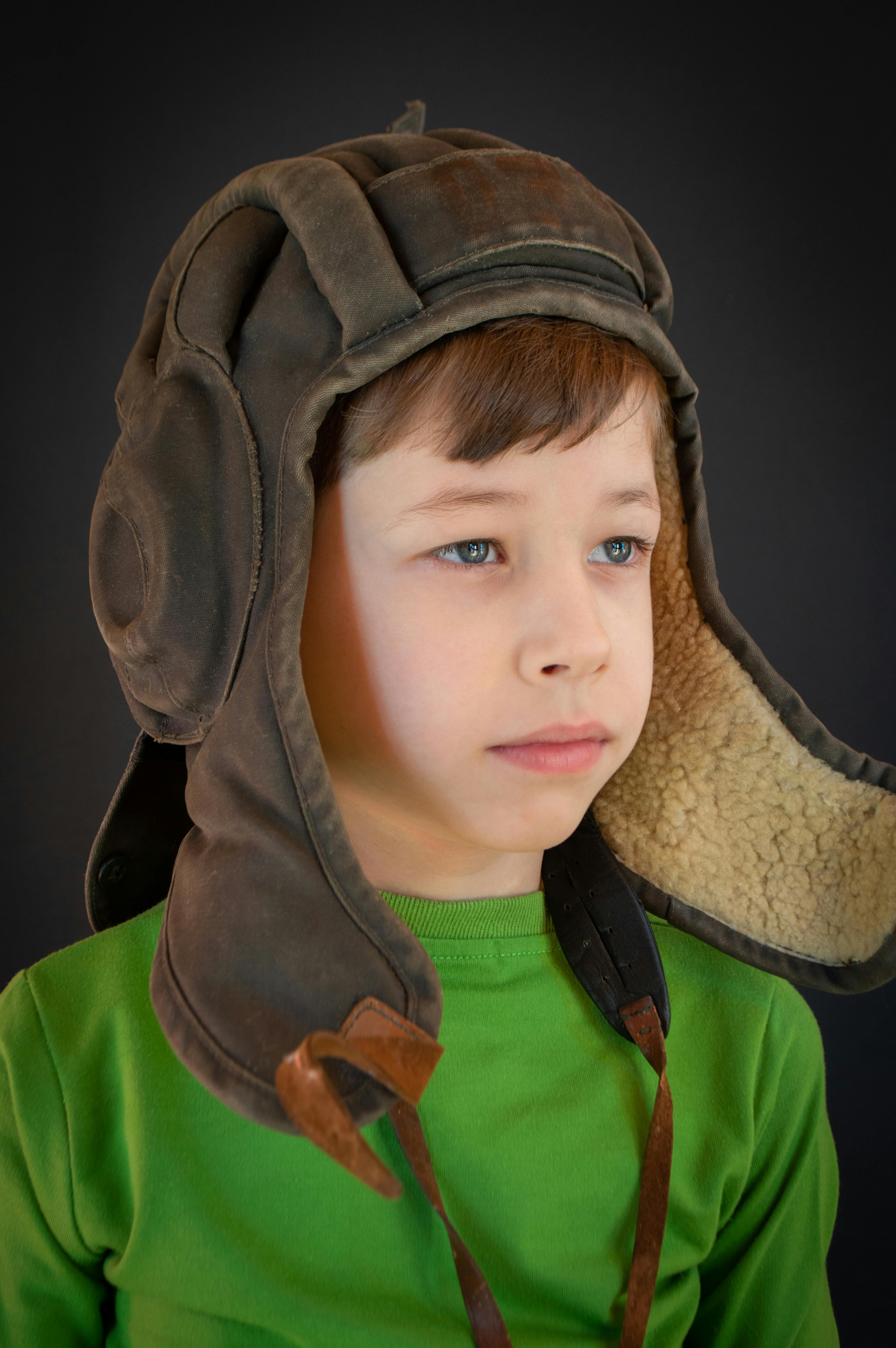 Portrait of a young boy wearing a vintage aviator hat with a thoughtful expression.