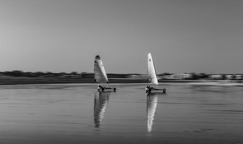 Grayscale Photo of Persons Land Sailing on Shore