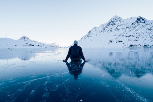 Free Man Sitting on Frozen Lake Looking at Mountains  Stock Photo