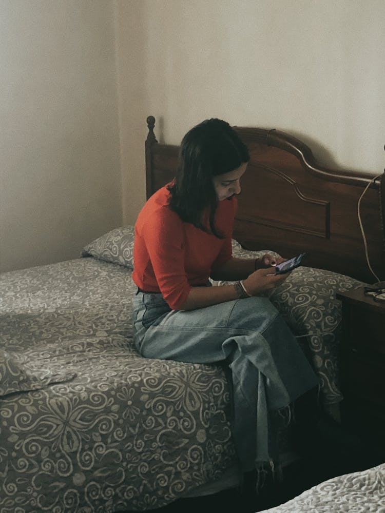 Woman In Red Sweater Sitting On Bedside Using Phone 