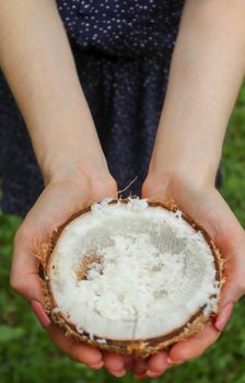 Hands holding a half coconut filled with shredded coconut outdoors.