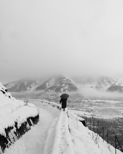 Monocohrome Photo of Person walking on a Snow-Covered Cliff