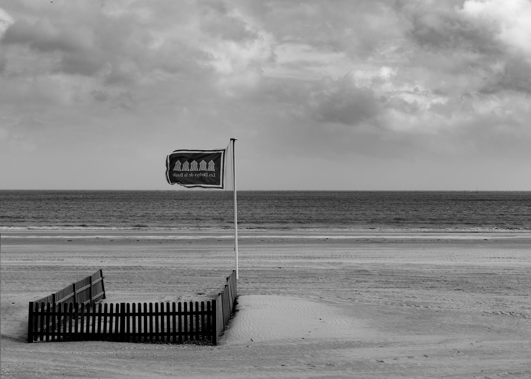A serene black-and-white view of La Baule beach with a flag and fence, capturing tranquility.