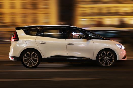Dynamic photo of a white minivan captured in motion during the night in Lisbon, Portugal.