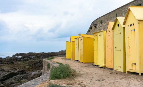 Vibrant yellow beach cabins line the rocky seaside of Batz-sur-Mer, France.