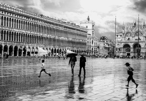 Black and white scene of people with umbrellas at St. Mark's Square, Venice, Italy.