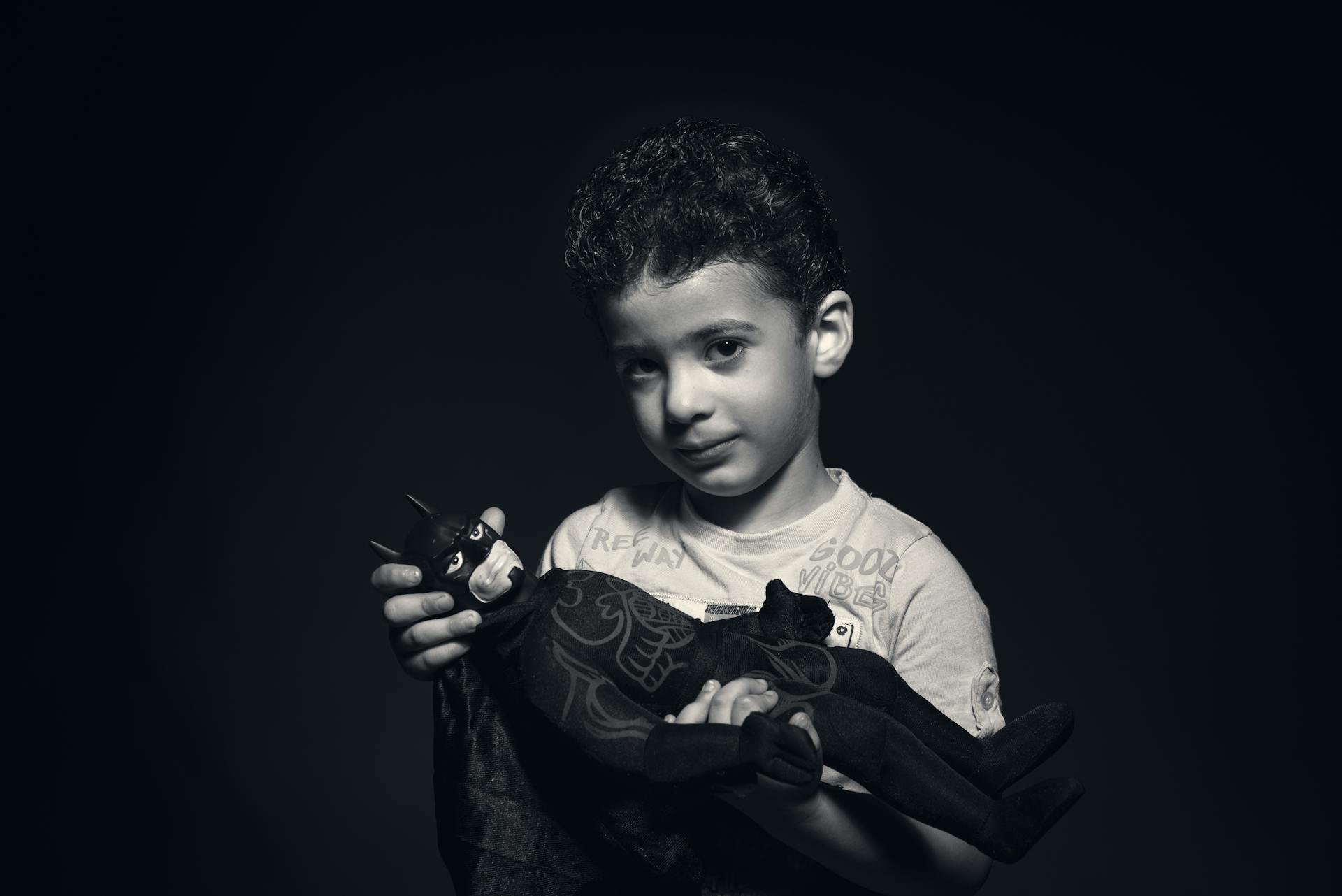 Grayscale Photo of a boy Holding Batman Plush Toy