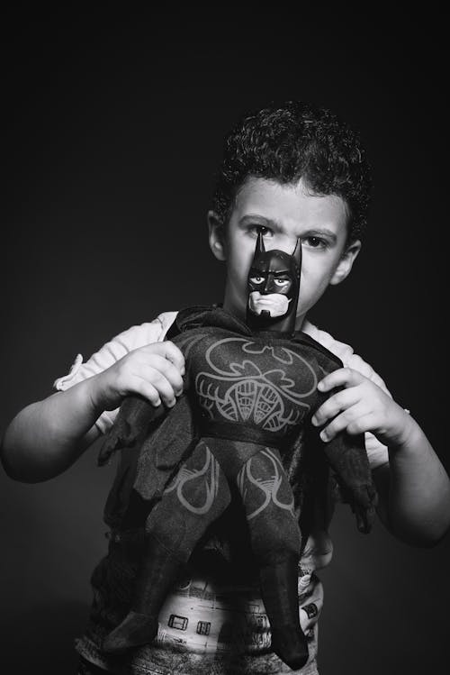 Grayscale Photo of Boy Holding Batman Plush Toy