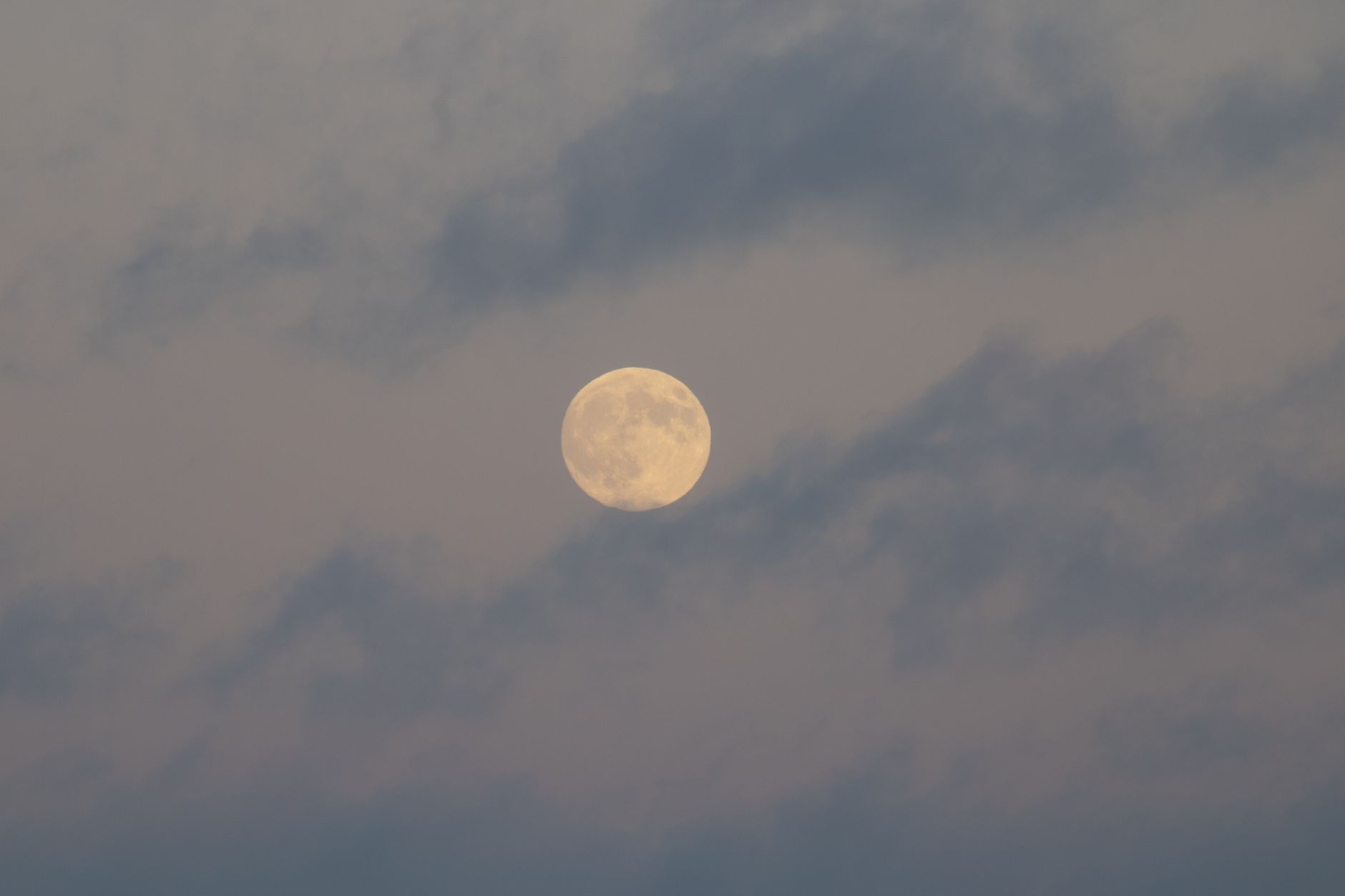 A tranquil full moon surrounded by soft, wispy clouds in a calm night sky.
