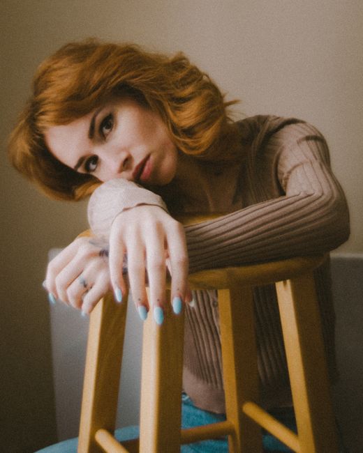 Artistic portrait of a redhead woman with a thoughtful expression, resting on a chair.