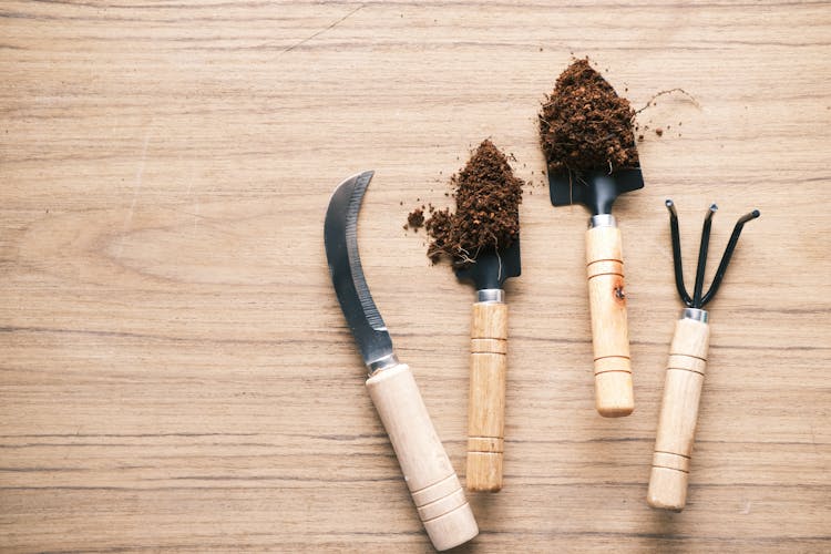 Garden Tools With Soil On Wooden Table