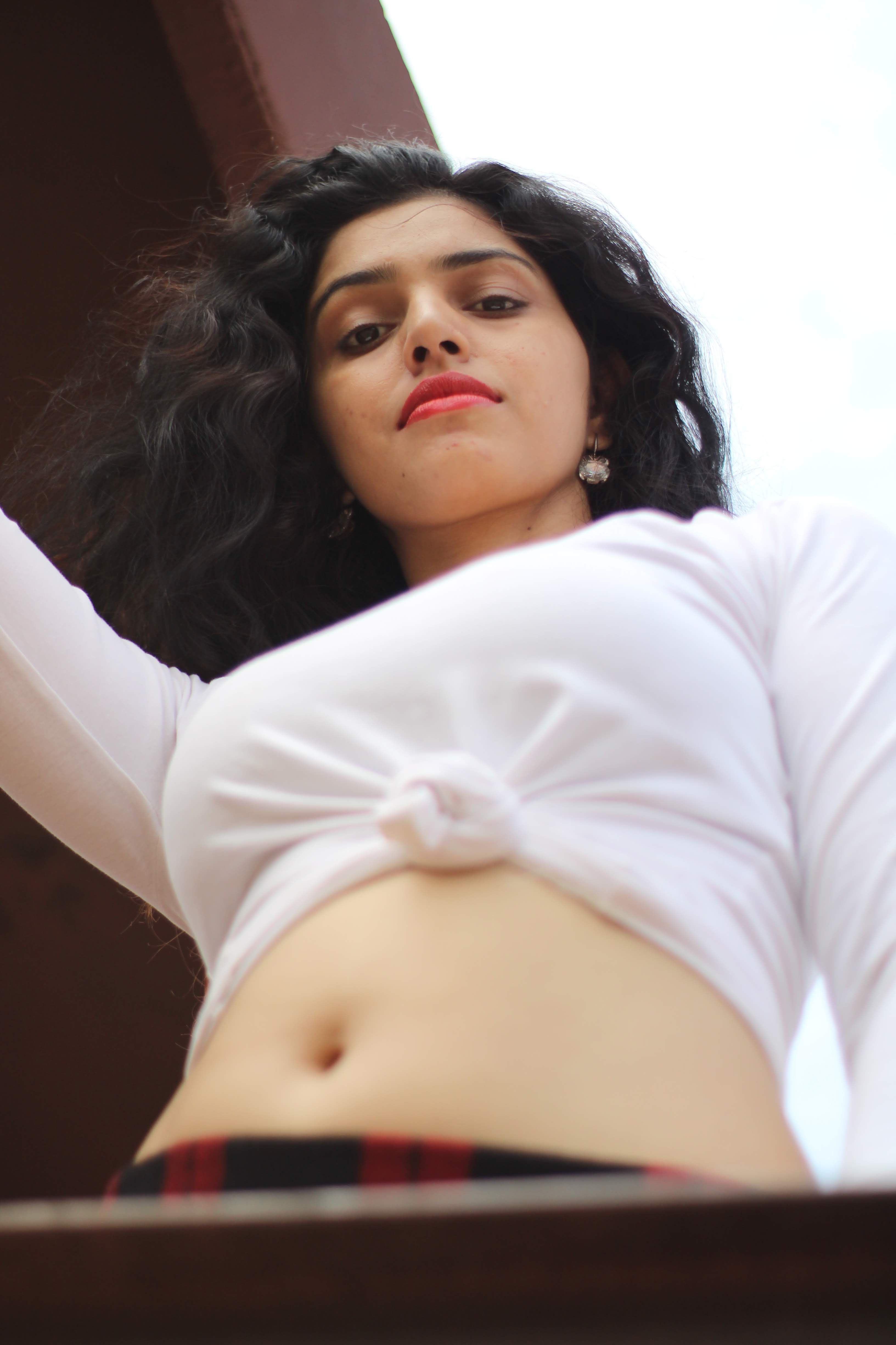 Young woman in a white crop top poses confidently, with red lipstick and curly hair.