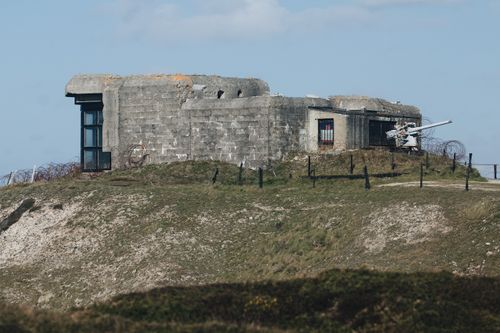 Free Abandoned WWII concrete bunker on a grassy hill under a clear blue sky. Stock Photo