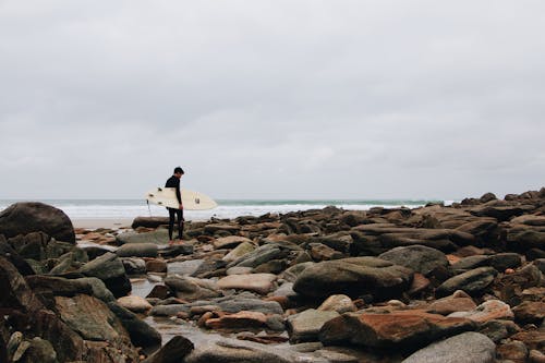 Free A Surfer Walking on Rocky Shore Stock Photo