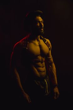 Portrait of a shirtless muscular man with dramatic lighting, emphasizing fitness and strength.