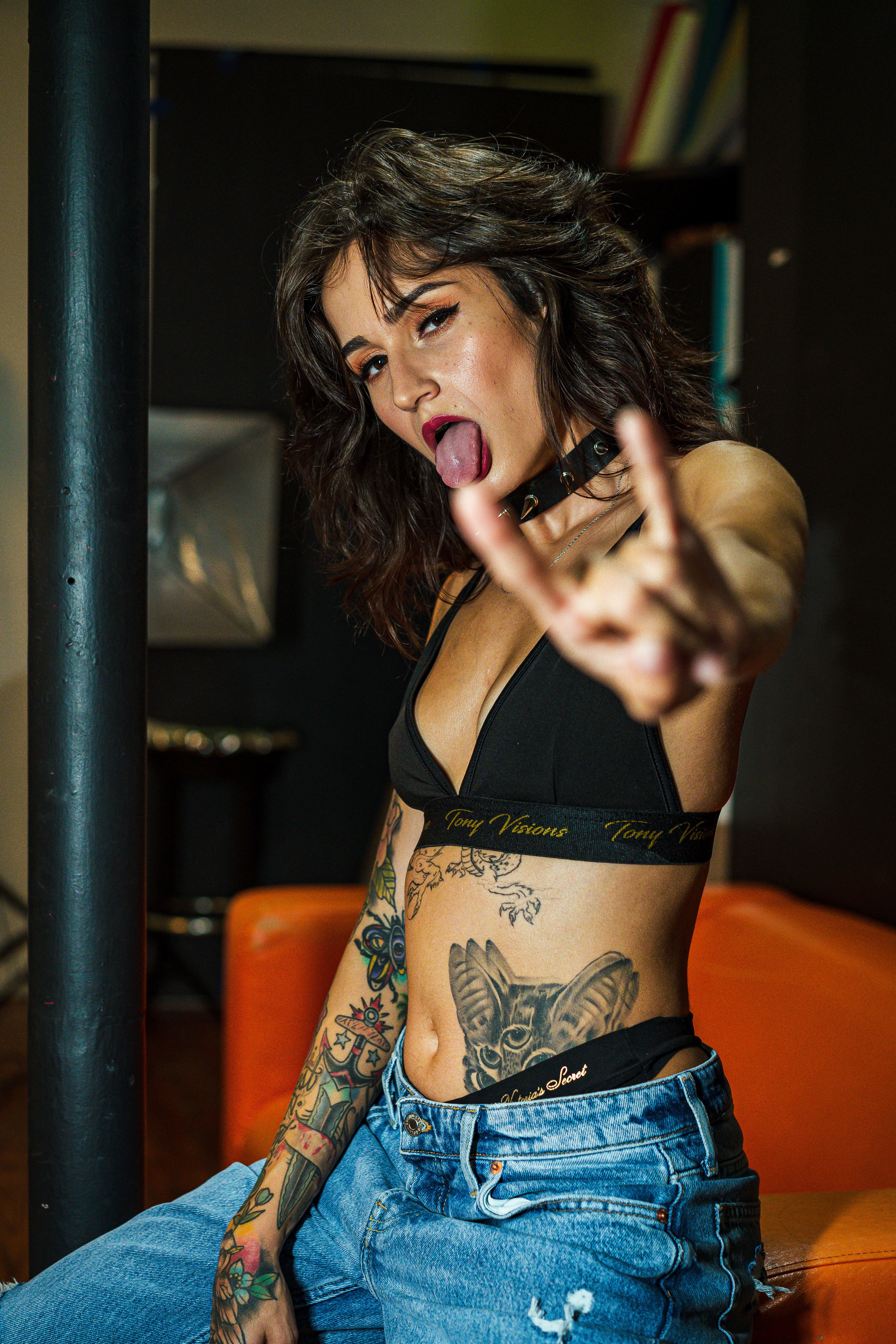 Stylish tattooed woman posing with rock hand gesture indoors.