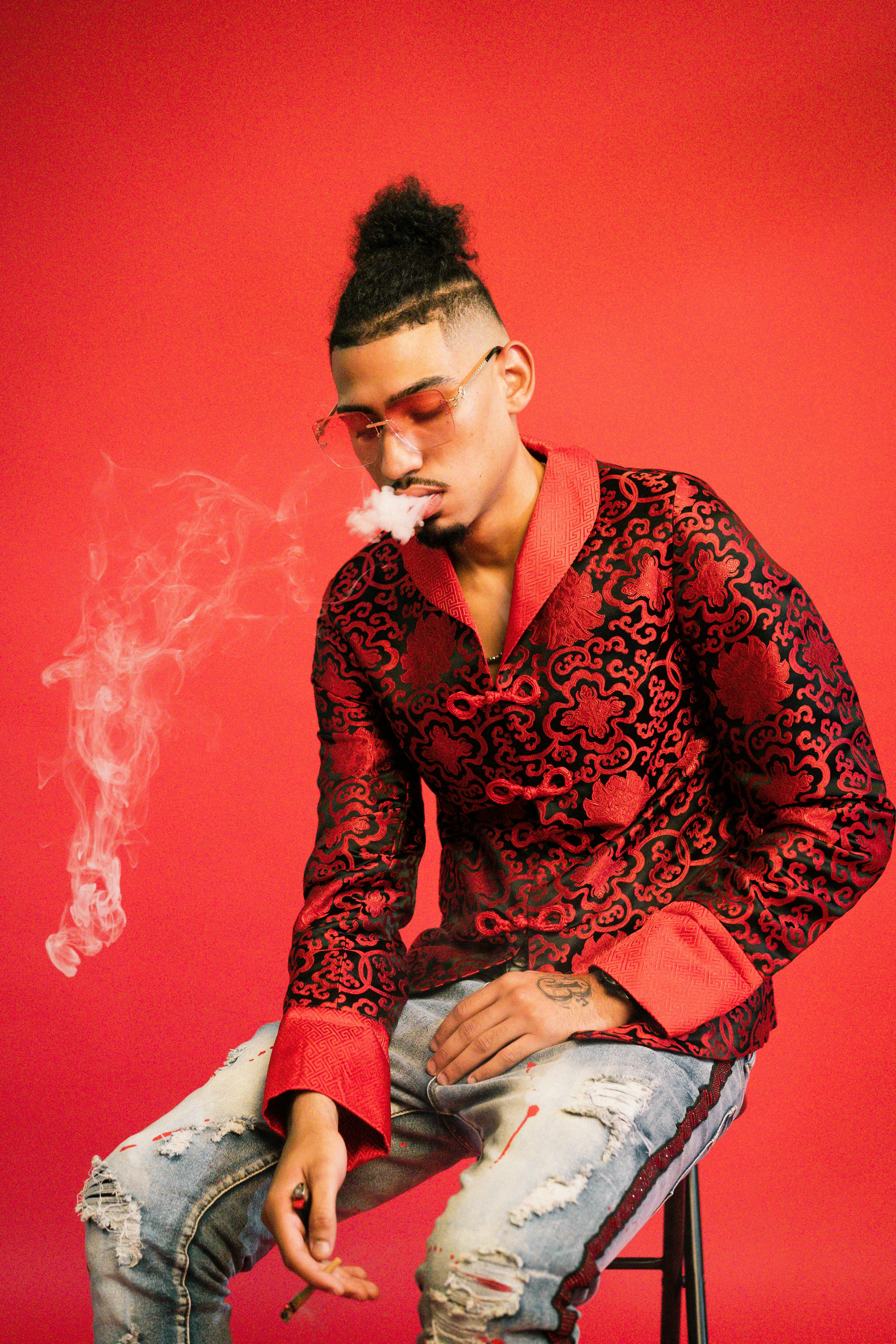 Fashion portrait of a man wearing glasses and smoking, set against a red background.