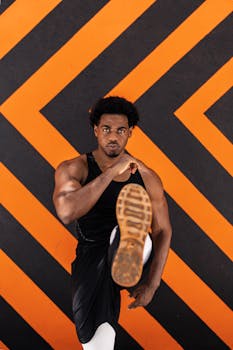 Athlete performing a powerful front kick against a striking black and orange geometric background.