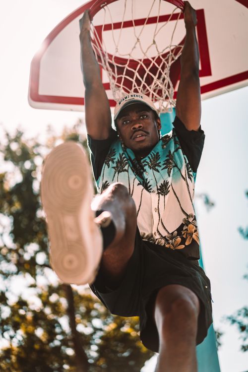 Free Young man performs a dynamic basketball dunk on an outdoor court. Stock Photo