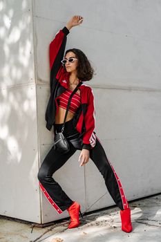 Fashionable woman in red and black outfit posing against a white wall.